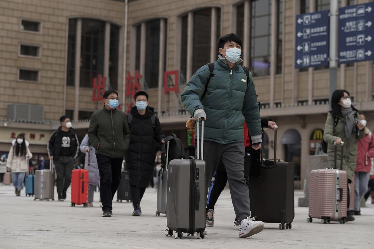 Arriving passengers in masks walk out of a Beijing railway station Tuesday.
