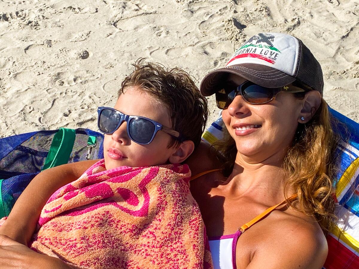 A mother and son lie on the sand at a beach