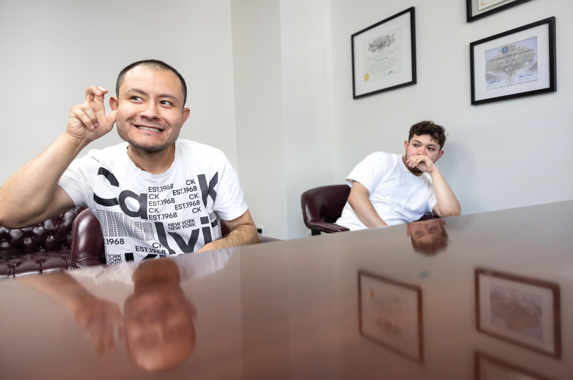 A man signs with his hands while his brother sits nearby in an office