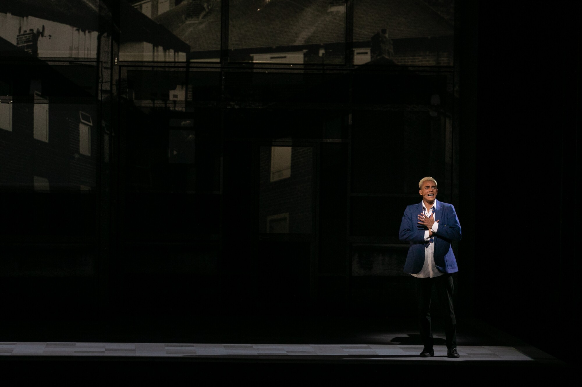 A man performs on a dark stage in a blue blazer.