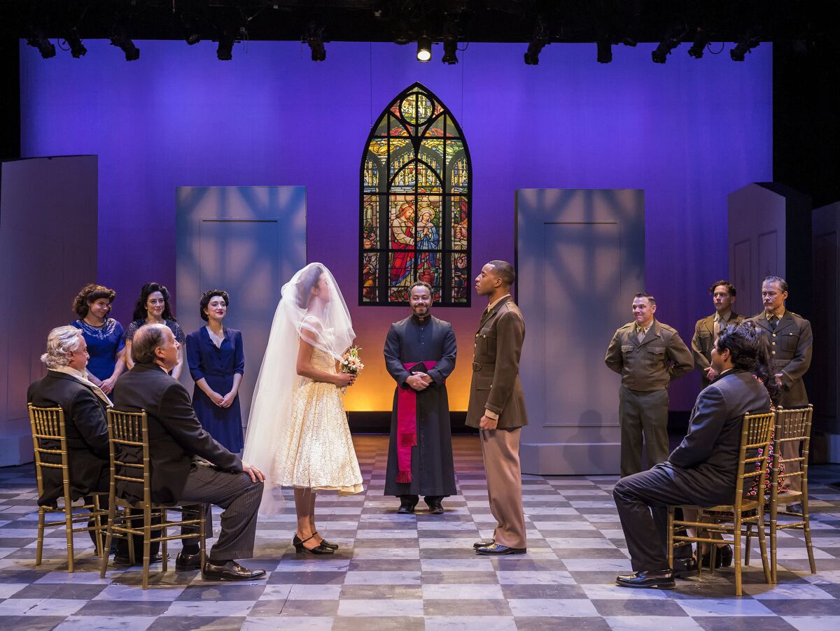 A woman in a bridal veil and man in soldier's uniform face each other in front of a stained-glass window.