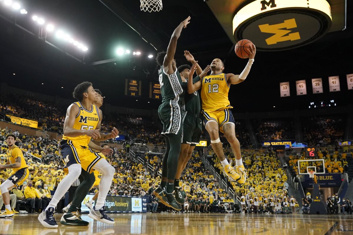 Michigan guard DeVante' Jones (12) attempts a layup as Michigan State center Mady Sissoko, left, and guard Jaden Akins, center, defend during the second half of an NCAA college basketball game, Tuesday, March 1, 2022, in Ann Arbor, Mich. (AP Photo/Carlos Osorio)
