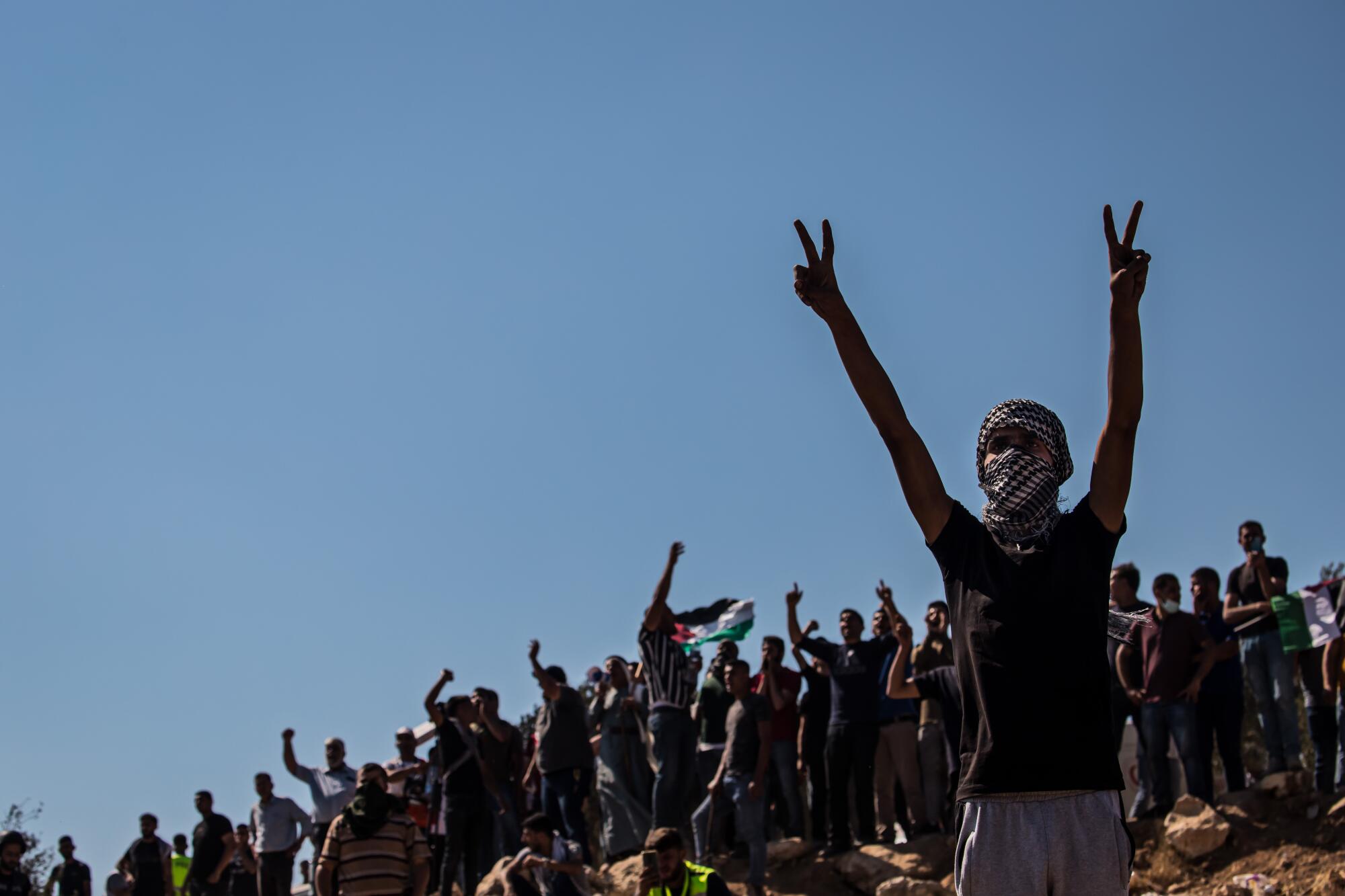 A Palestinian raises his arms in front of a line of protesters chanting slogans at Israeli soldiers