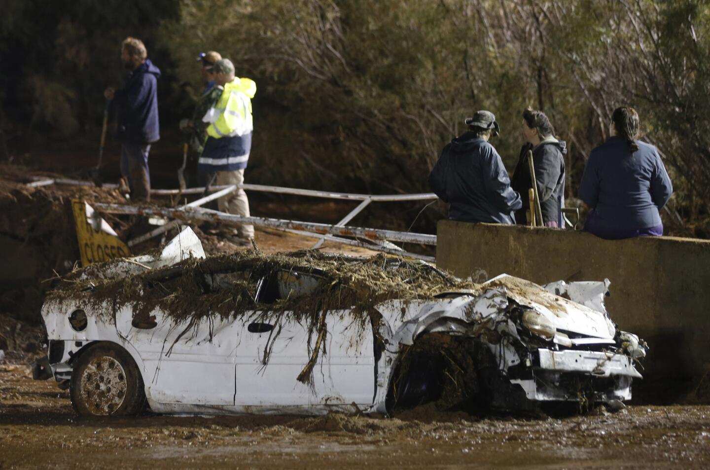 A car sits on the side of the road after being pulled from Short Creek as rescuers and others watch large construction equipment remove flood debris from Short Creek where it crosses Central Street in Hildale, Utah.