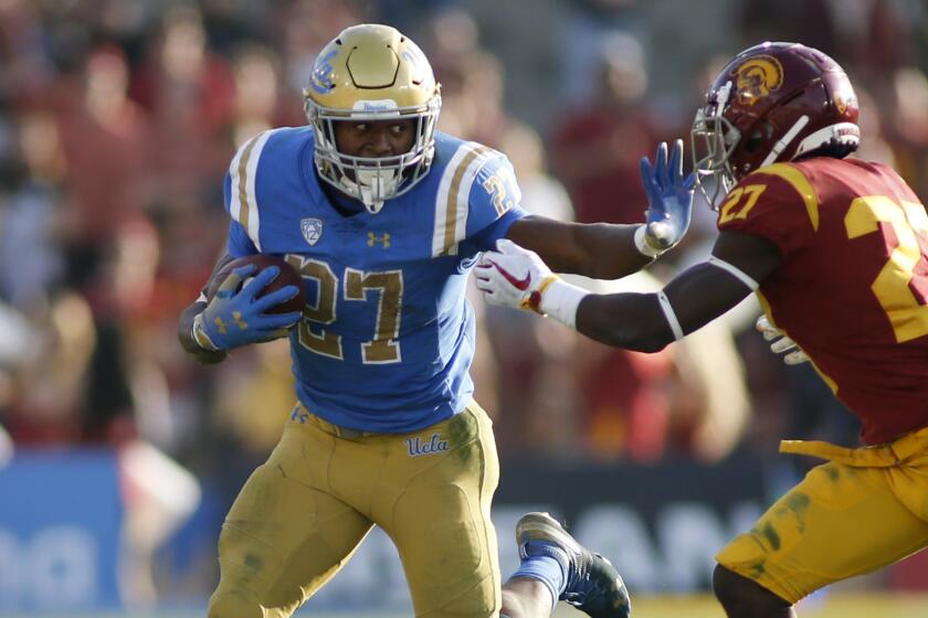 PASADENA, CALIFORNIA - NOVEMBER 17: Running back Joshua Kelley #27 of the UCLA Bruins pushes off cornerback Ajene Harris #27 of the USC Trojans during the second half of a football game at Rose Bowl on November 17, 2018 in Pasadena, California. (Photo by Katharine Lotze/Getty Images)