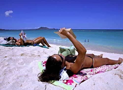 Two sunbathers get lost in books on a lazy day at the 2 1/2 -mile-long beach at Kailua Bay.