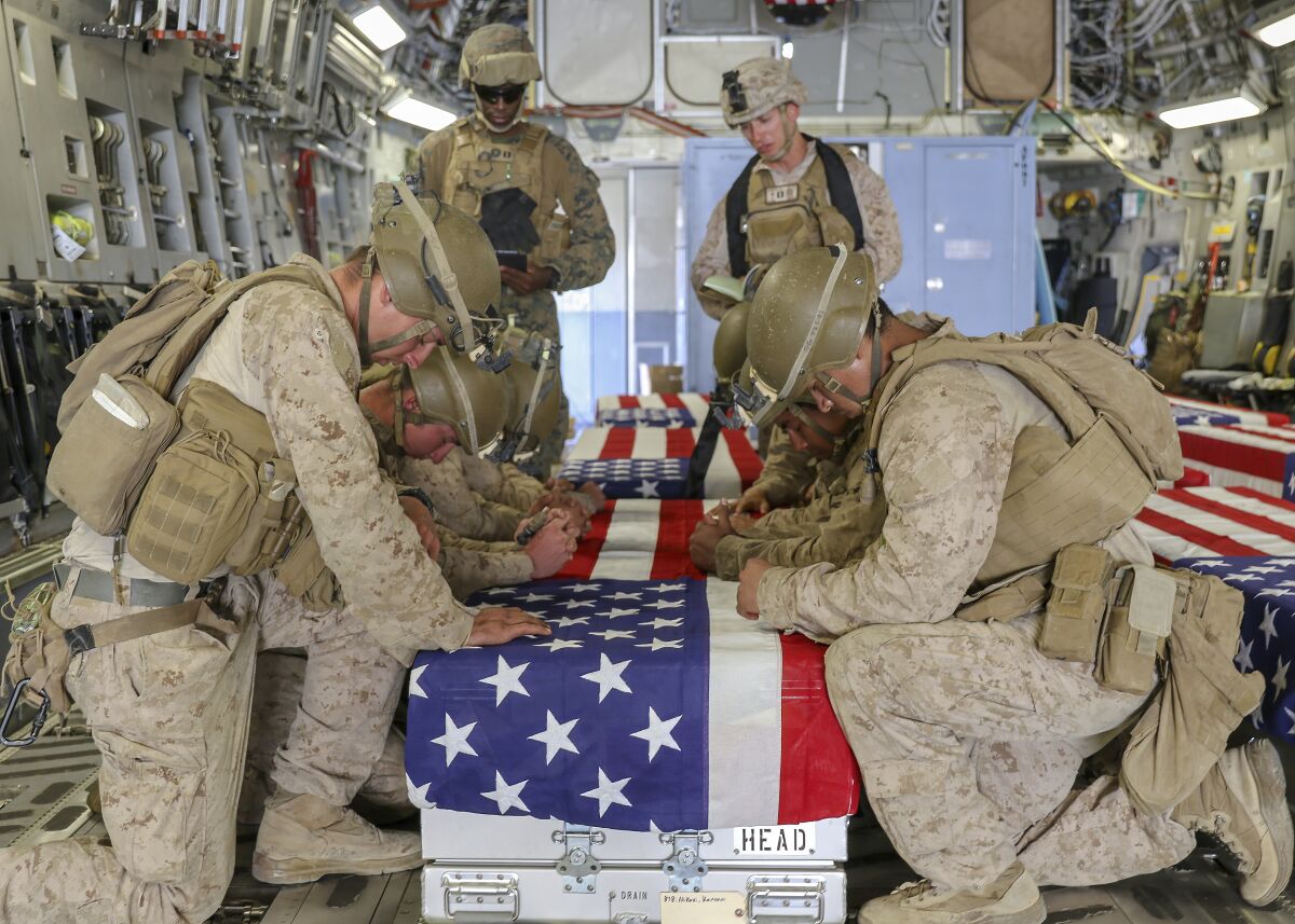 Troops kneel around boxes with U.S. flags draped on them