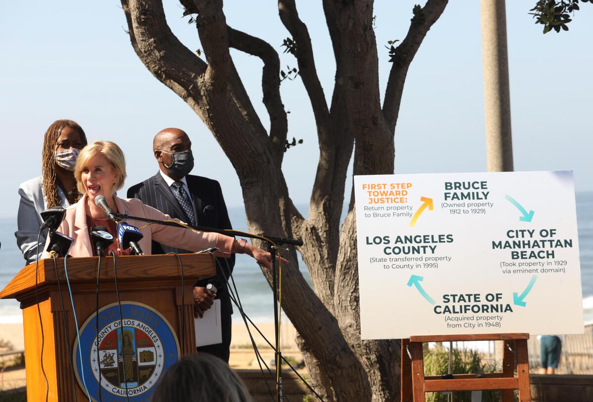 Three people at a lectern beside a sign depicting the ownership history of Bruce's Beach.