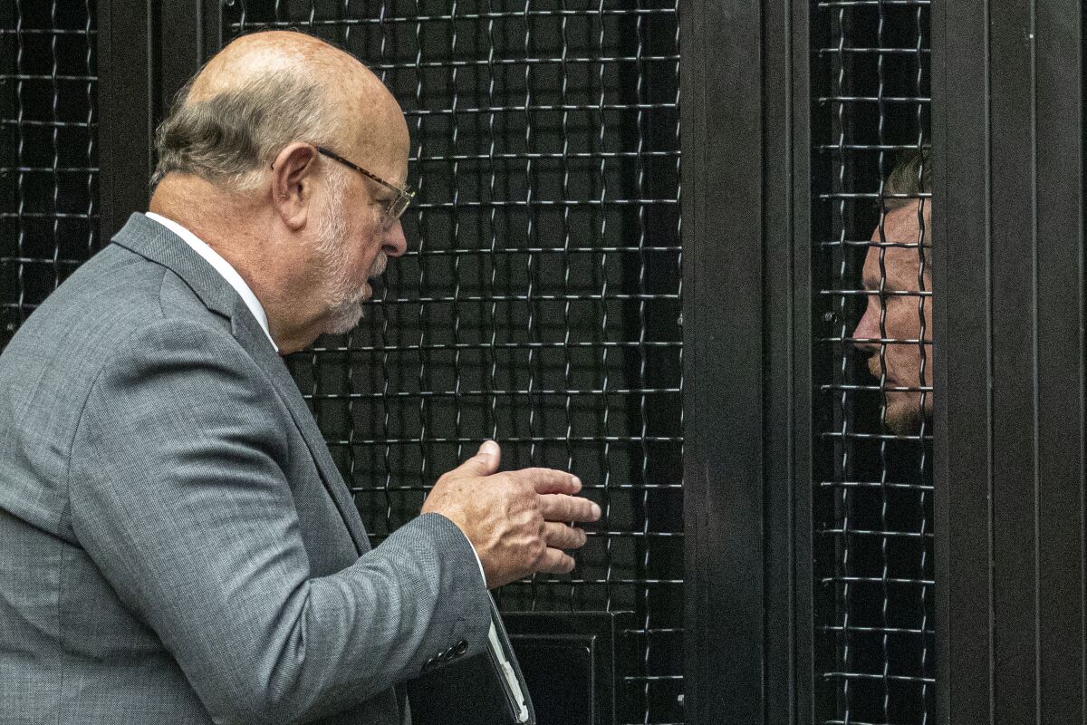 An attorney speaks to his client through a cage in a courtroom