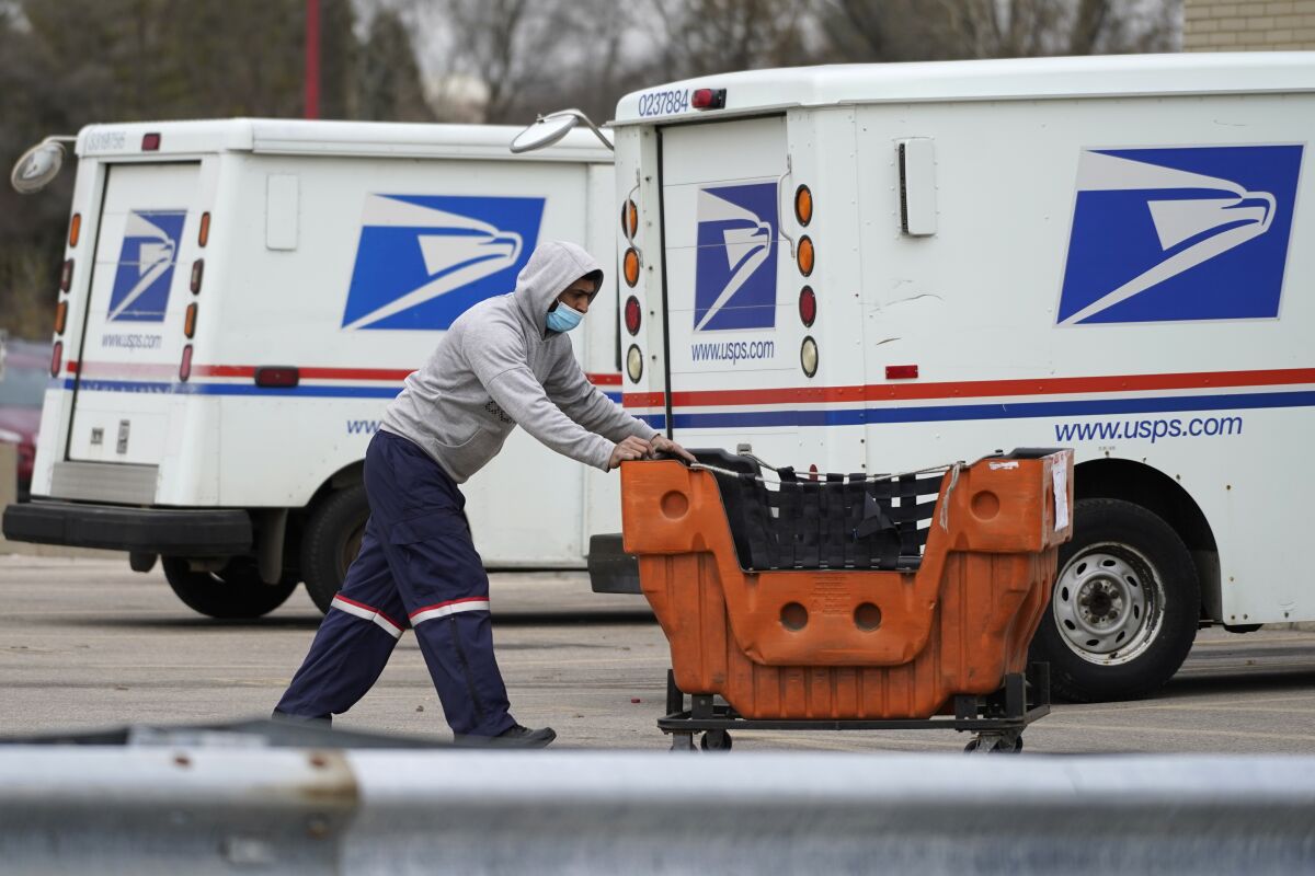 A United States Postal Service employee pushes a bin outside.