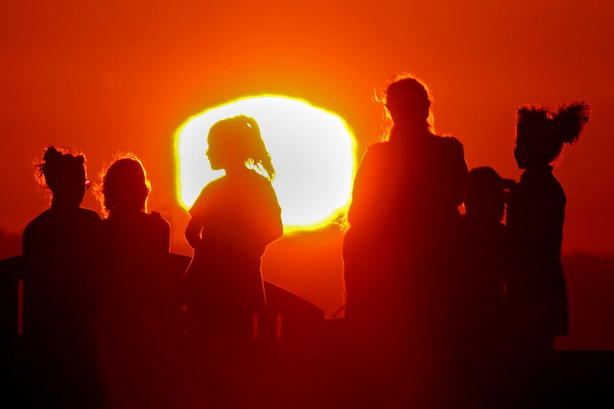 Six people are silhouetted against a red sky and setting sun.