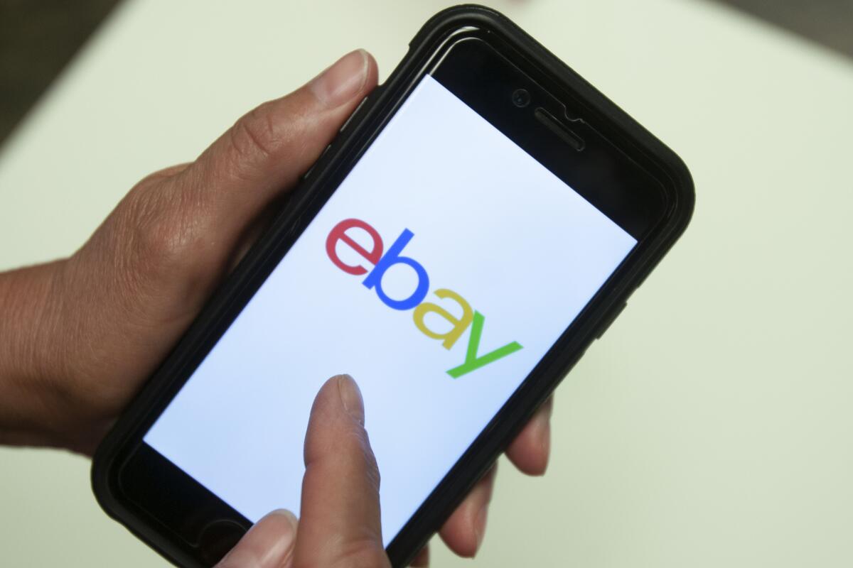 A person holds a smartphone displaying the EBay app