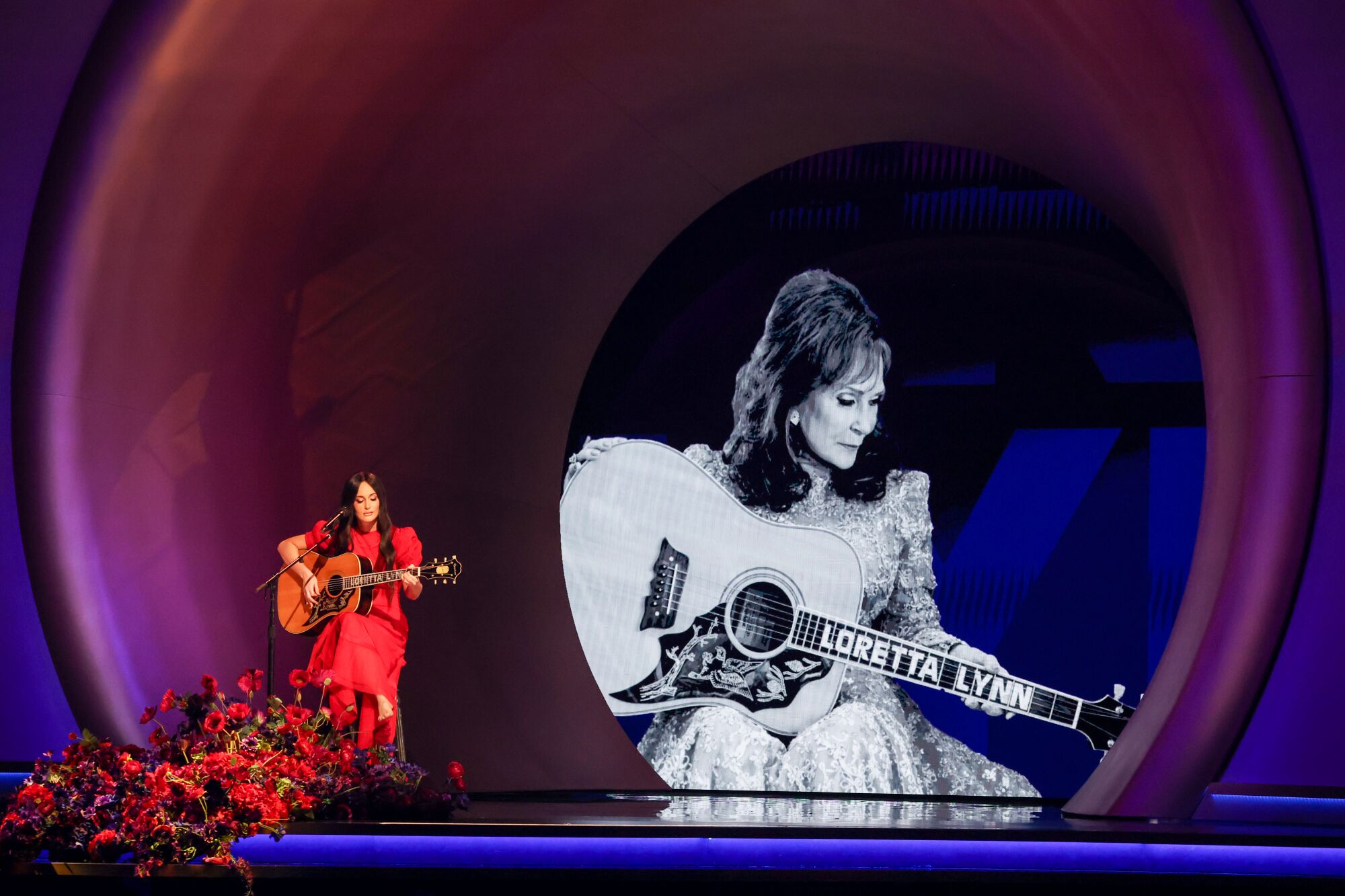 Une femme assise et jouant de la guitare devant un micro et une image géante en noir et blanc d'une femme jouant de la guitare