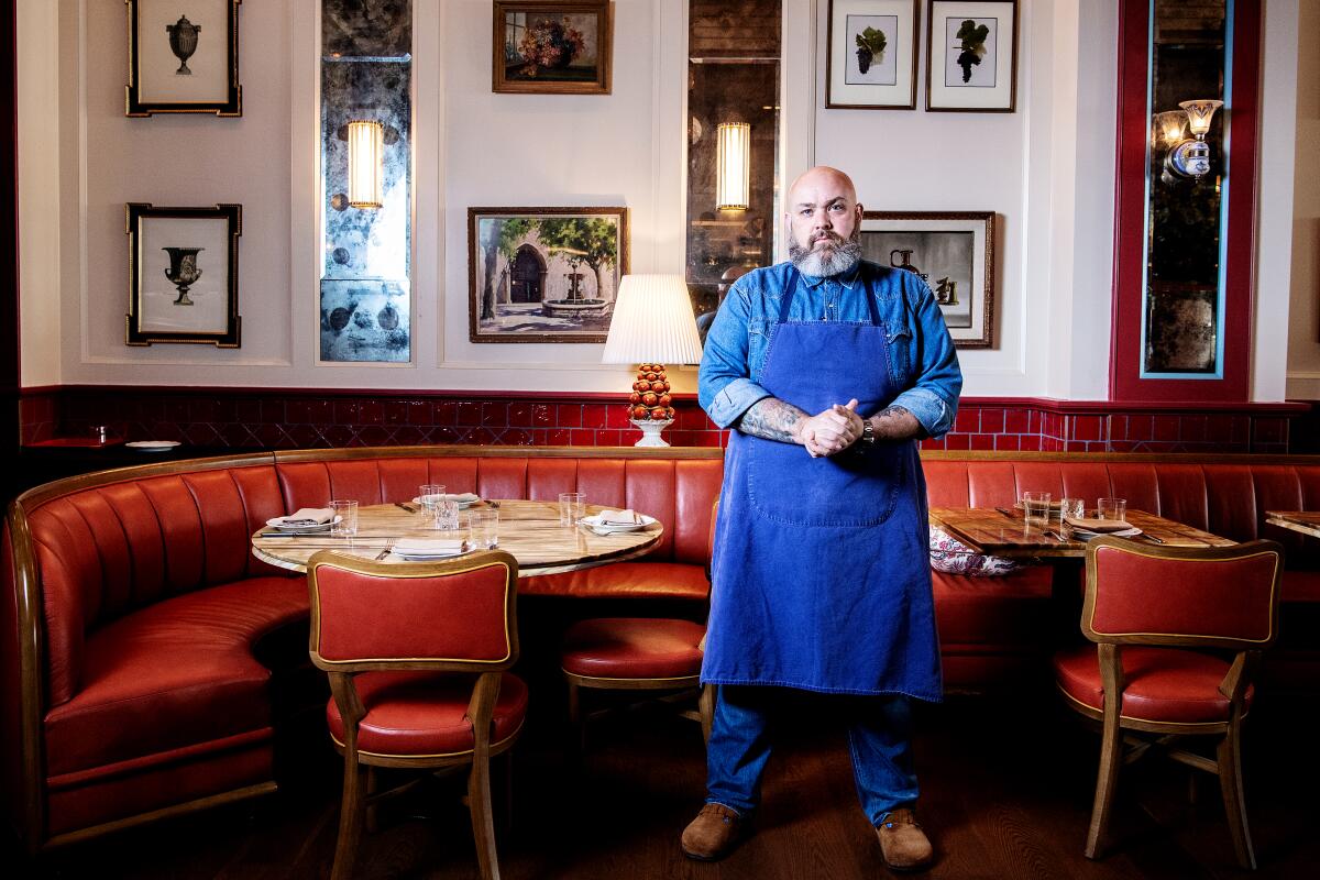 A man stands in front of red banquette booths and a wall of framed artwork.