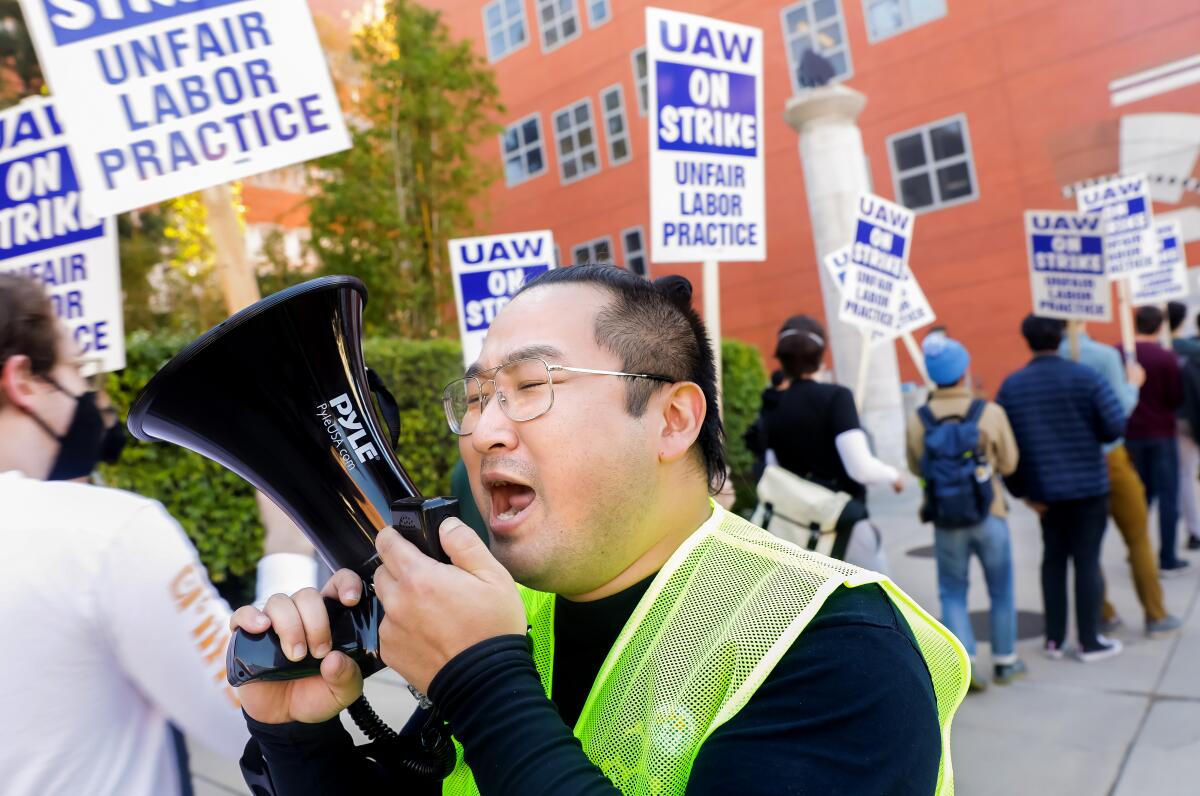 A man speaks into a megaphone. Behind him are people marching with signs.