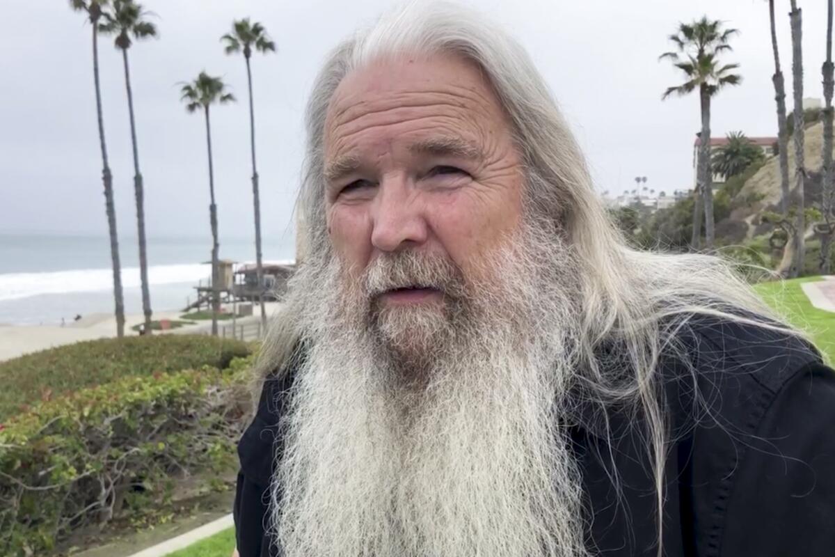 Robert Claypool, with a long white beard, stands near the beach San Clemente.
