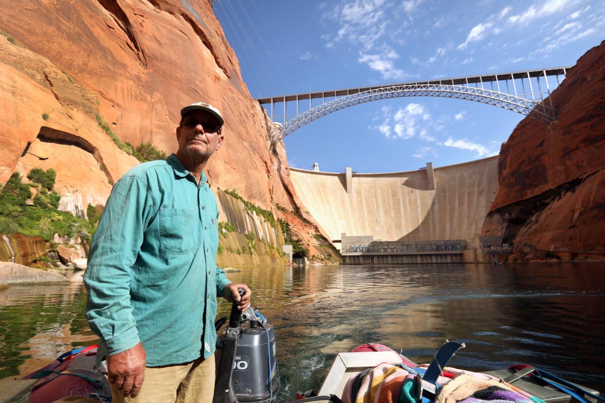 A man stands in a boat with a dam in the background. 