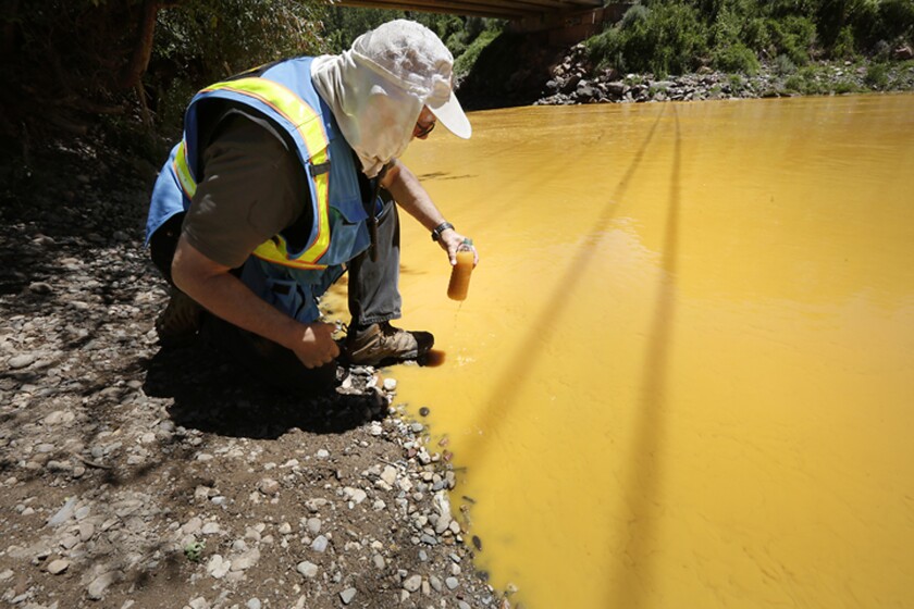 FILE - In this Aug. 6, 2015, file photo, Dan Bender of the La Plata County Sheriff's Office takes a water sample from the Animas River near Durango, Colo., after the accidental release of an estimated 3 million gallons of waste from the Gold King Mine. The Navajo Nation's Department of Justice announced on Wednesday, Jan. 13, 2021, has settled with two mining companies to resolve claims stemming from a 2015 spill that sent wastewater downstream from the inactive Gold King Mine in southwestern Colorado. (Jerry McBride/The Durango Herald via AP, File)
