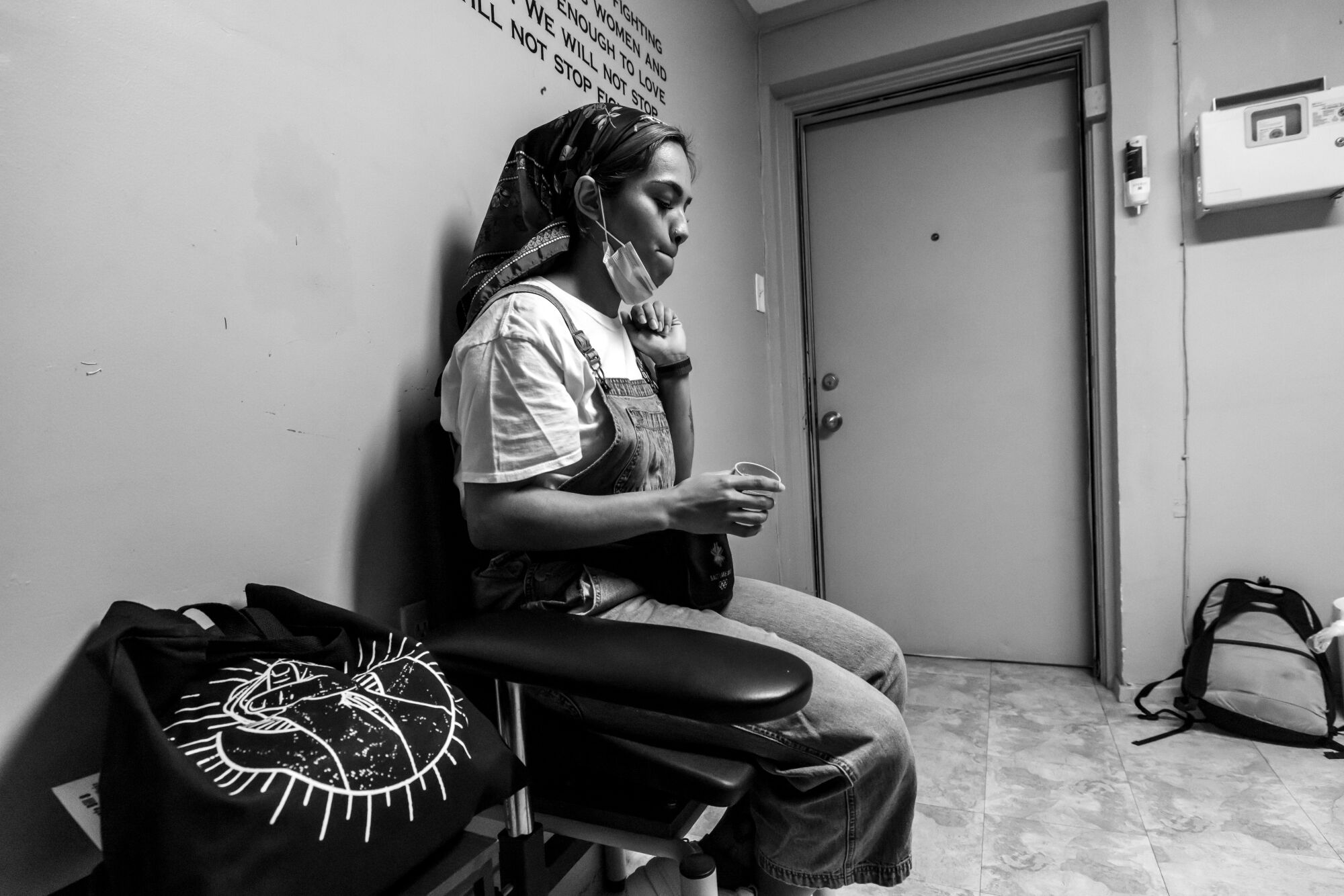 A woman sits in an exam room on a chair against a wall