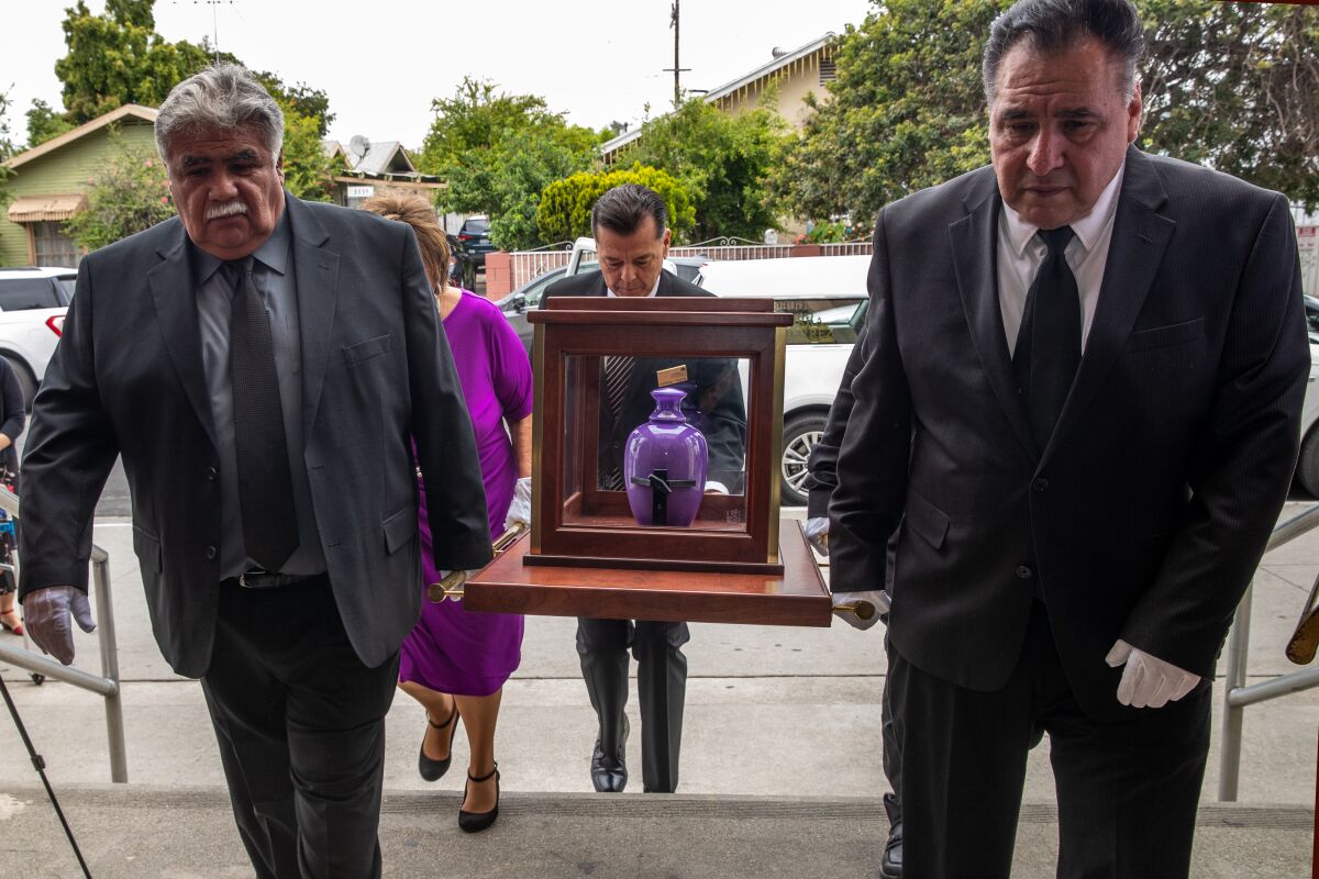 Pallbearers, two brothers in front and sister, bring urn carrying ashes of Gloria Molina at funeral services.
