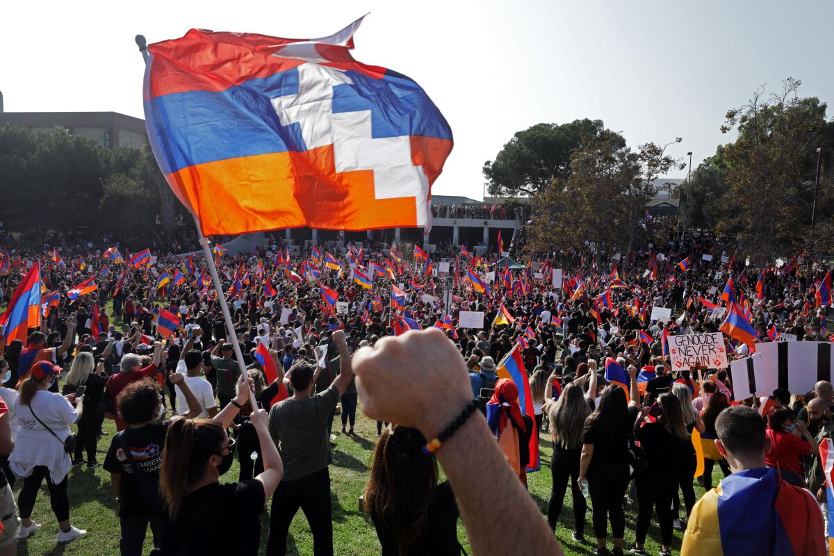 Protesters with red blue and orange Armenian flags raise their fists in a park