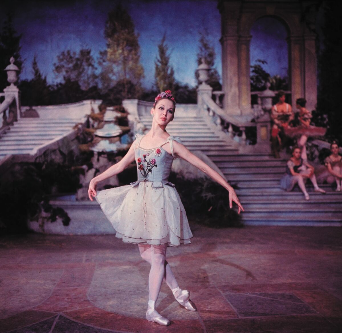 A ballerina with one hand holding her tutu skirt on stage