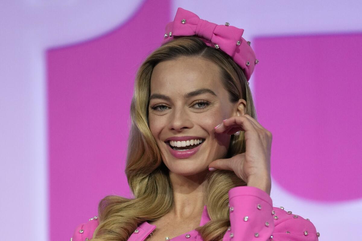Margot Robbie wears a pink blazer and hat with sliver specks as she poses for photos.