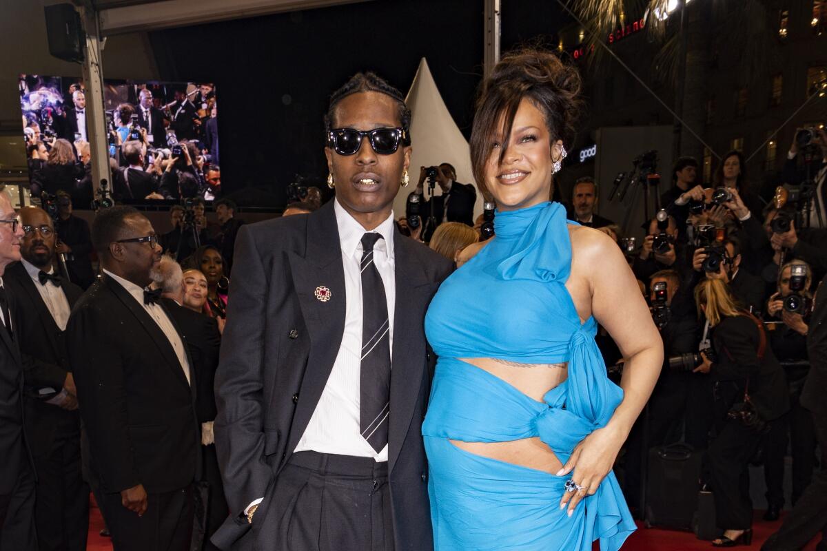 ASAP Rocky in a suit and sunglasses posing next to Rihanna in a blue cut-out gown.
