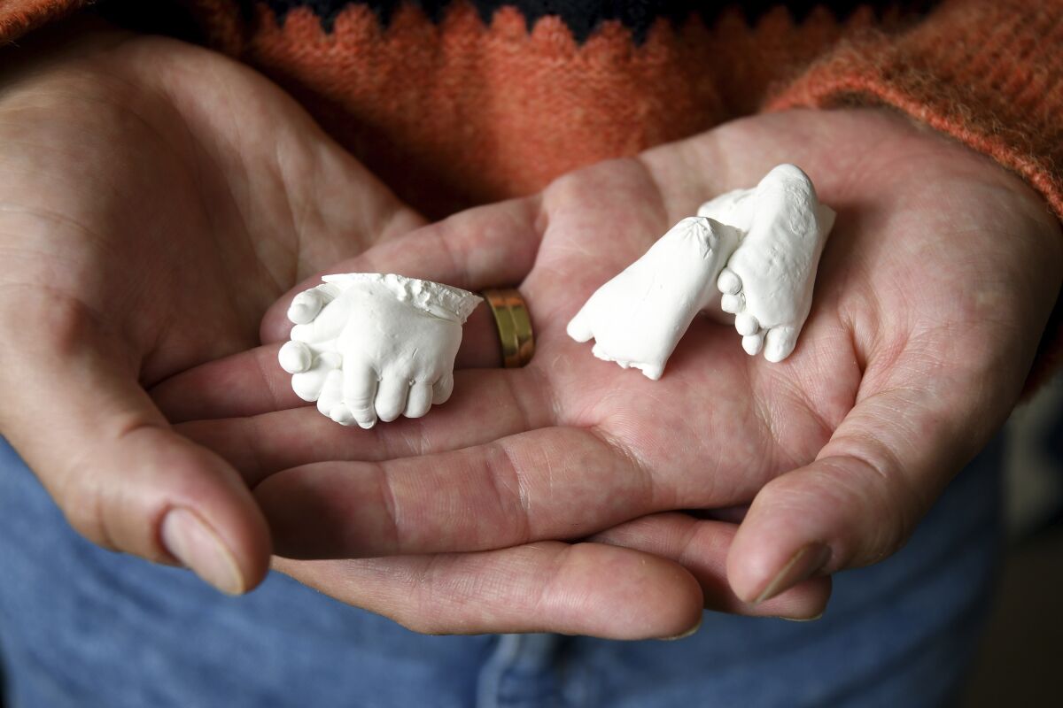Christina Taylor holds plaster casts of her baby's hands and feet at her home in Littleton, Colo., on Wednesday, April 27, 2022. Taylor chose to get an abortion when she found out after 20 weeks that her baby had no kidneys or bladder. Taylor said she honors her loss with the casts, which were made by the hospital's bereavement team. (AP Photo/Thomas Peipert)