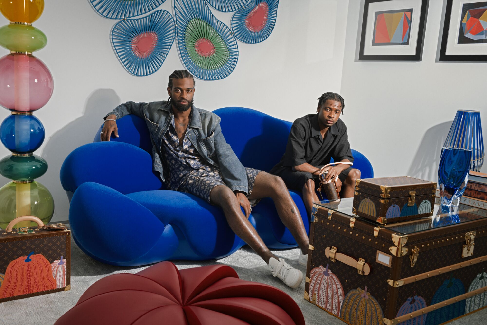 Two people sit on a blue couch in a room with Louis Vuitton suitcases.