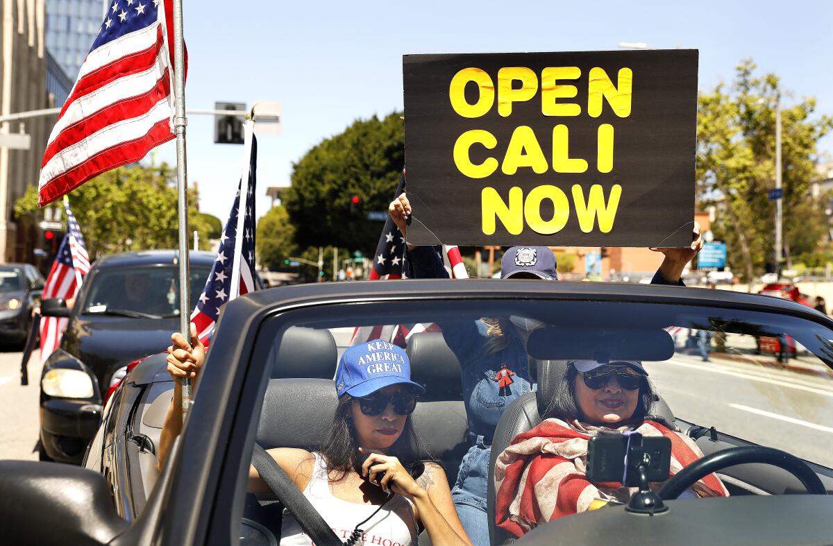 A group of protesters, including Alma Villanueva, left, and Gigi Wilcox, right, stage a vehicle caravan protest April 22 in downtown Los Angeles calling on state and local officials to reopen the economy.