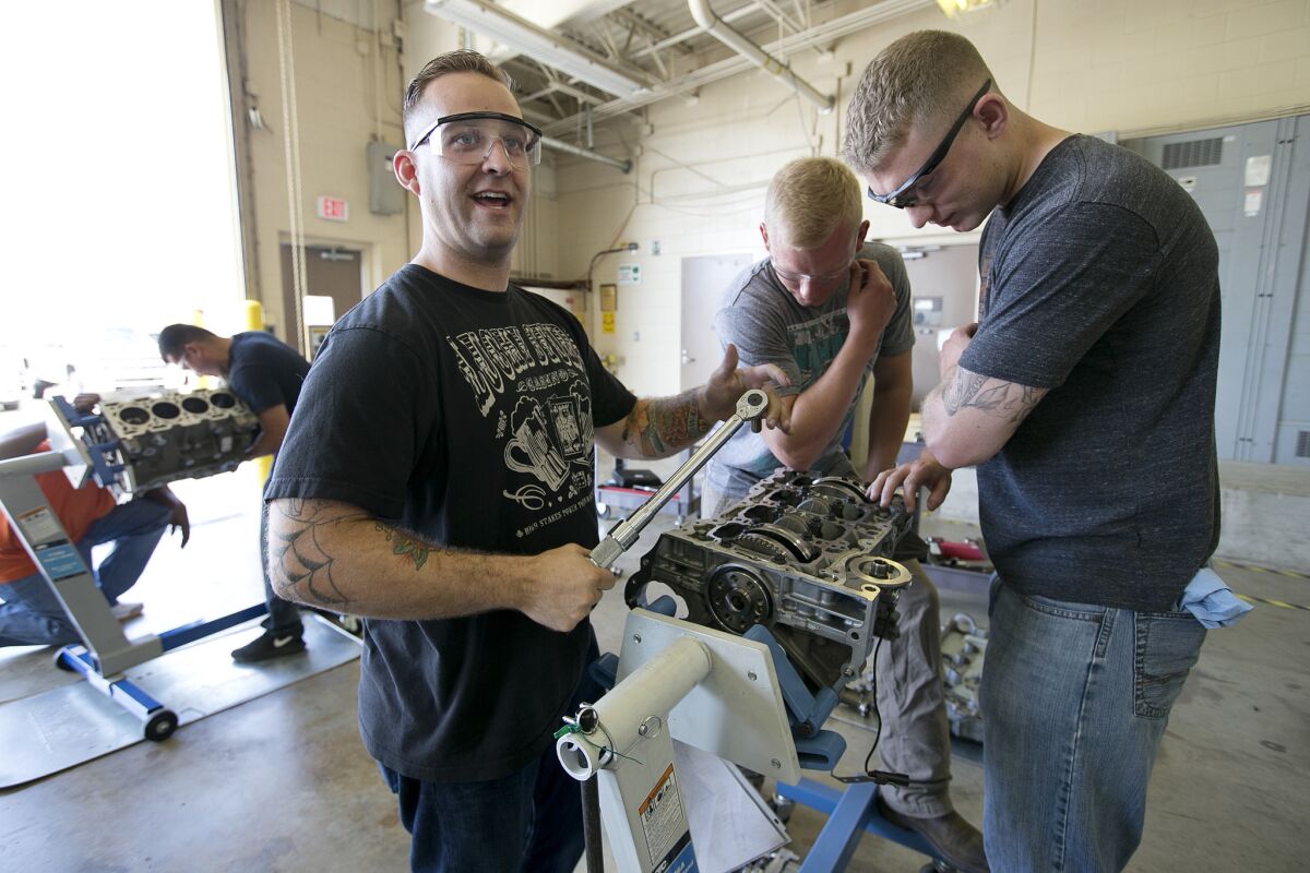 Army Sgt. Garret Baganz, left, Spec. Tyler Sonsoucie, center, and Spec. Ian Sokol work on an ecotech engine at Ft. Hood, Texas, on June 18 as part of a GM program that teaches auto skills.
