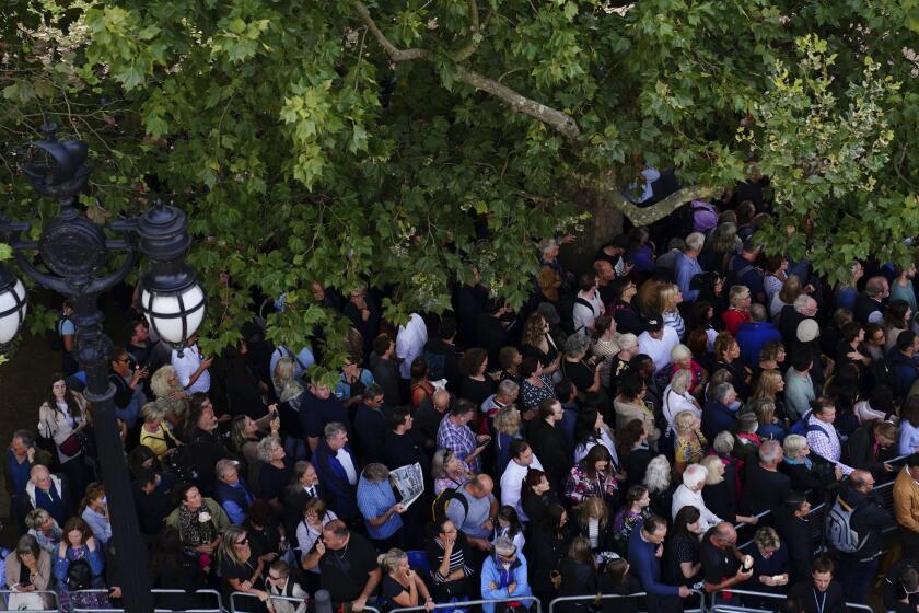 Crowds gather along The Mall ahead of the procession of the coffin of Queen Elizabeth II from Buckingham Palace to Westminster Hall, London, Wednesday Sept. 14, 2022. The Queen will lie in state in Westminster Hall for four full days before her funeral on Monday Sept. 19. (Victoria Jones/Pool via AP)
