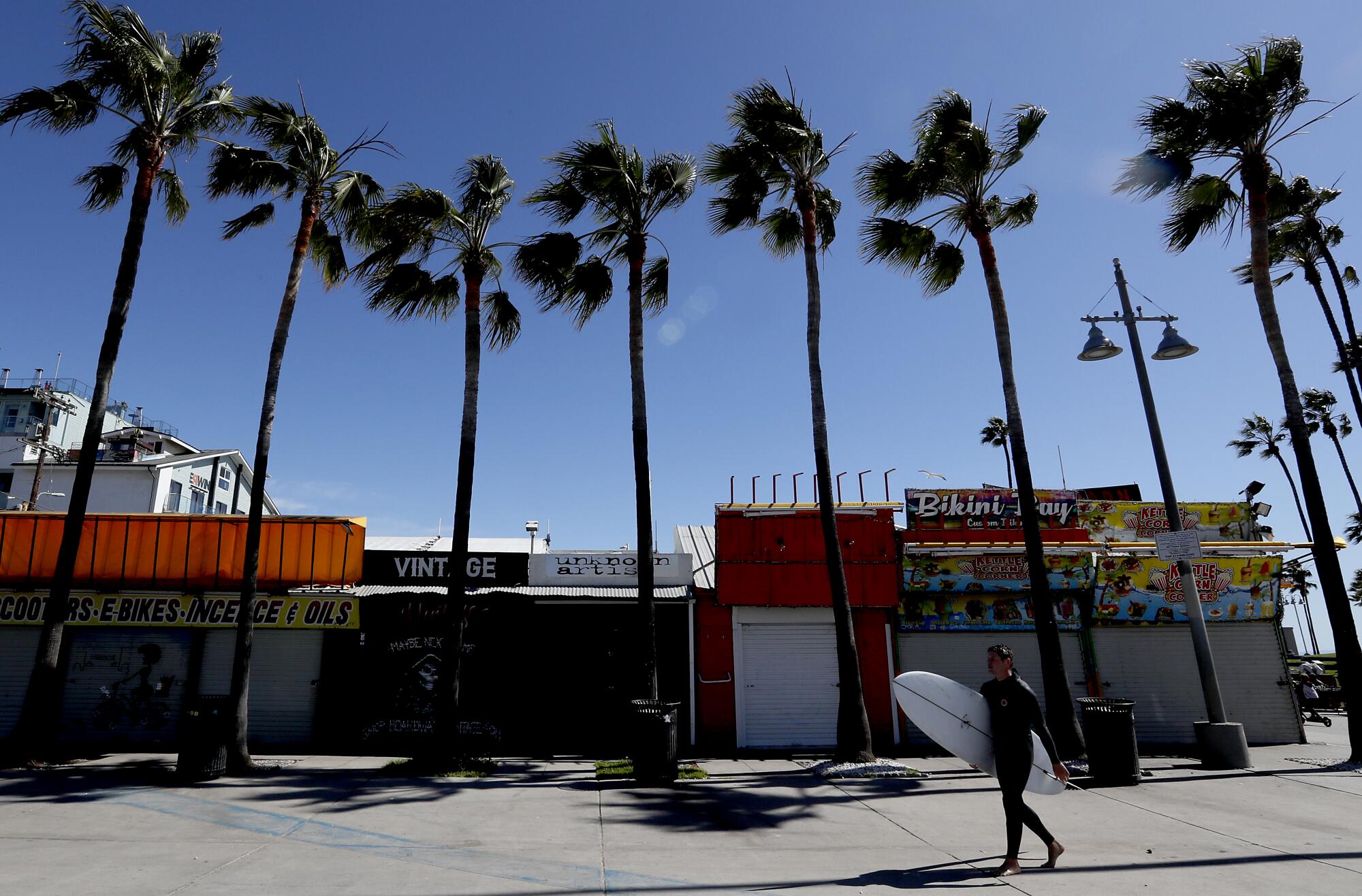 A surfer walks past shuttered shops on Windward Avenue in Venice Beach.