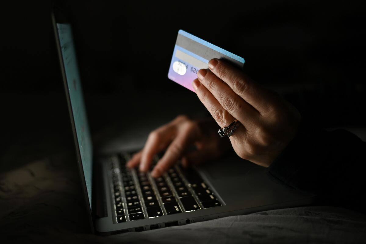 A person holds a credit card while shopping online on a computer