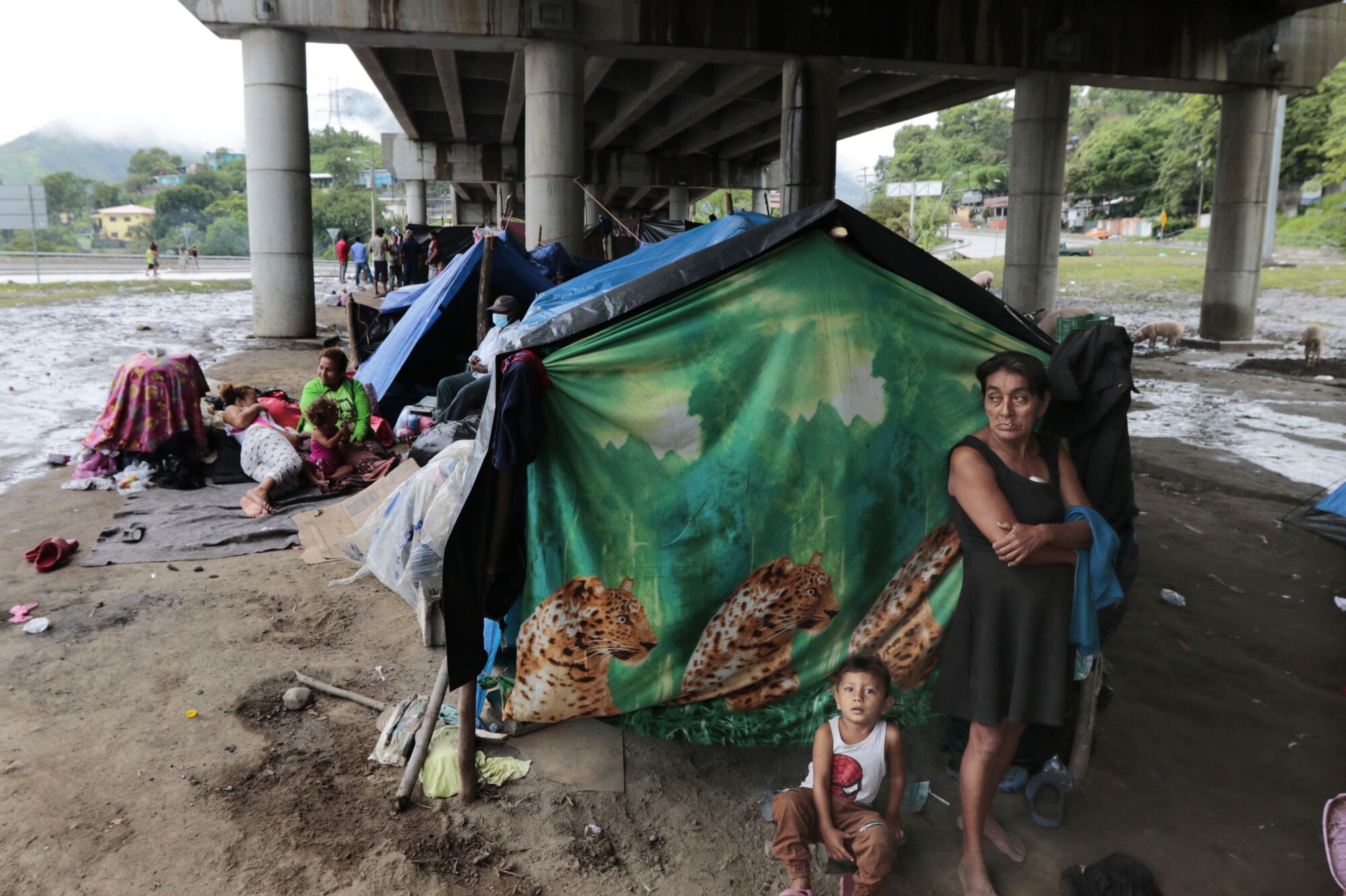 A woman and small boy stand in front of a makeshift tent under a bridge in San Pedro Sula, Honduras