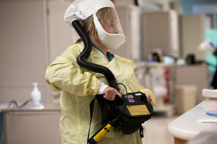 KIRKLAND WASHINGTON MARCH 14, 2020 - A health care worker at EvergreenHealth puts on a powered air purifying respirator, also known as a PAPR) as she prepares to care for patients suspected of having COVID-19 in the negative pressure emergency department in Kirkland, WA on March 14, 2020. A hose attached to battery unit around her waist pumps clean air into her hood. (photo by Karen Ducey)