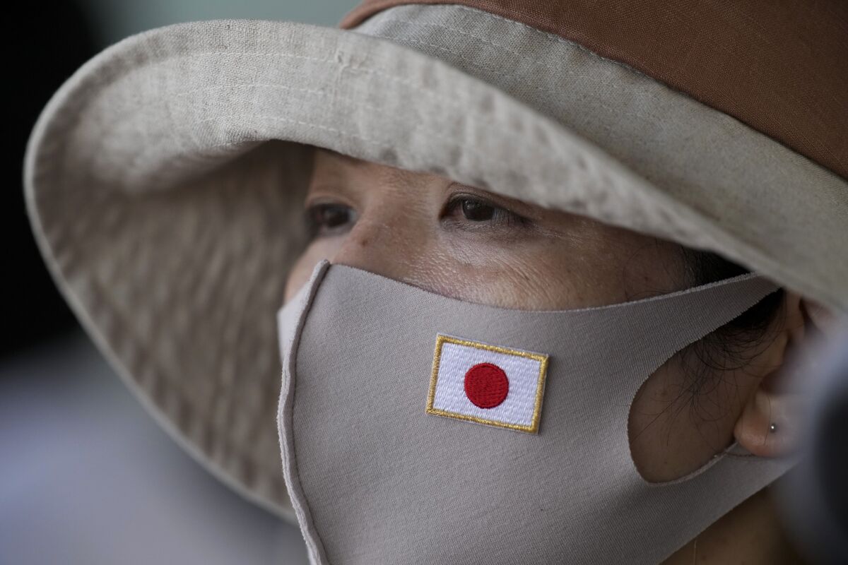 A spectator wears a mask bearing the flag of Japan while watching the men's cycling road race at the 2020 Summer Olympics, Saturday, July 24, 2021, in Oyama, Japan. (AP Photo/Christophe Ena)