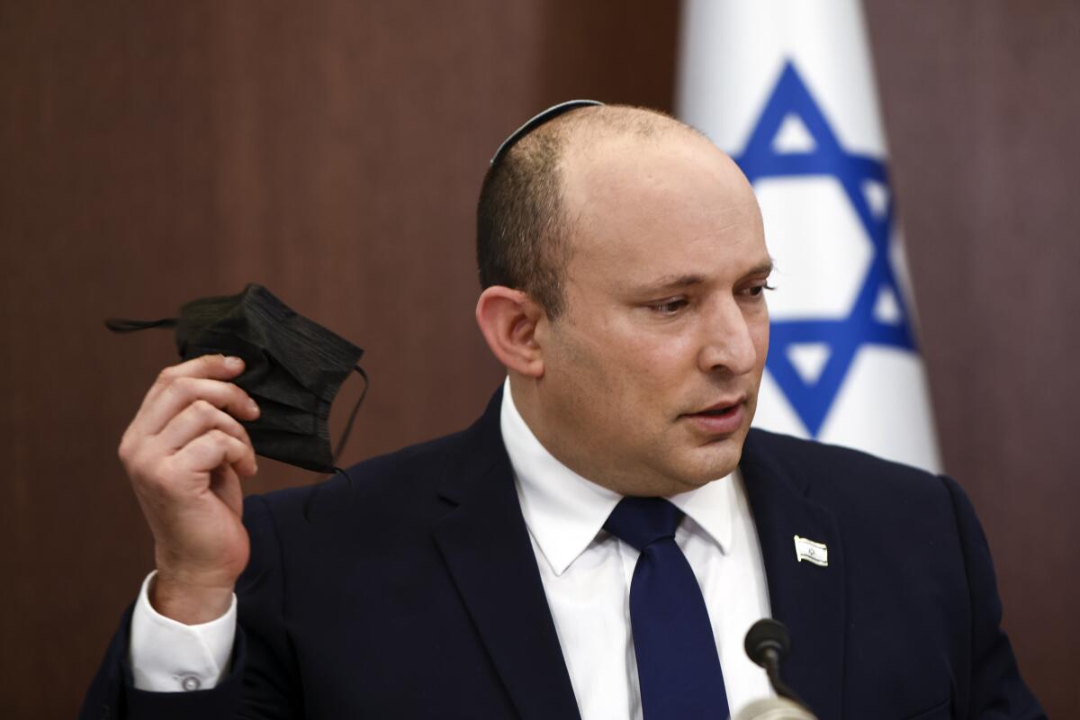 FILE - In this Oct. 5, 2021 file photo, Israeli Prime Minister Naftali Bennett holds his face mask at the weekly cabinet meeting in Jerusalem. Bennett will travel for the first time as premier to meet Russian President Vladimir Putin later this month, in the seaside resort city of Sochi. (Ronen Zvulun/Pool via AP, File)