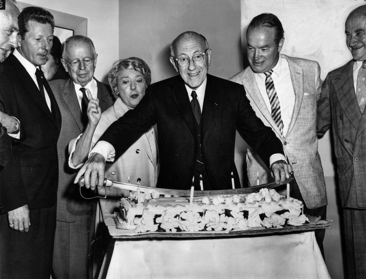 Aug. 12, 1958: Movie pioneer Cecil B. De Mille uses saber to cut 77th birthday cake at Paramount studio party.