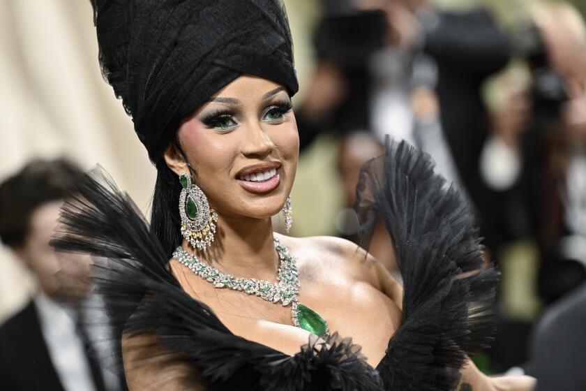 Cardi B wears a black turban, large ruffled gown and emerald-green pendant