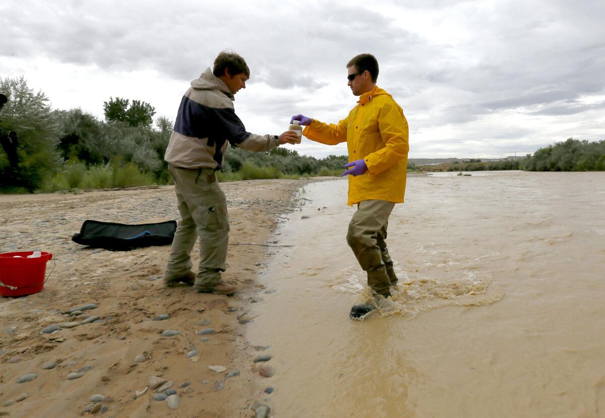 Ben Brown with the Utah Department of Environmental Quality, left, receives a San Juan River sample from hydrologic technician Ryan Parker in Montezuma Creek, Utah.