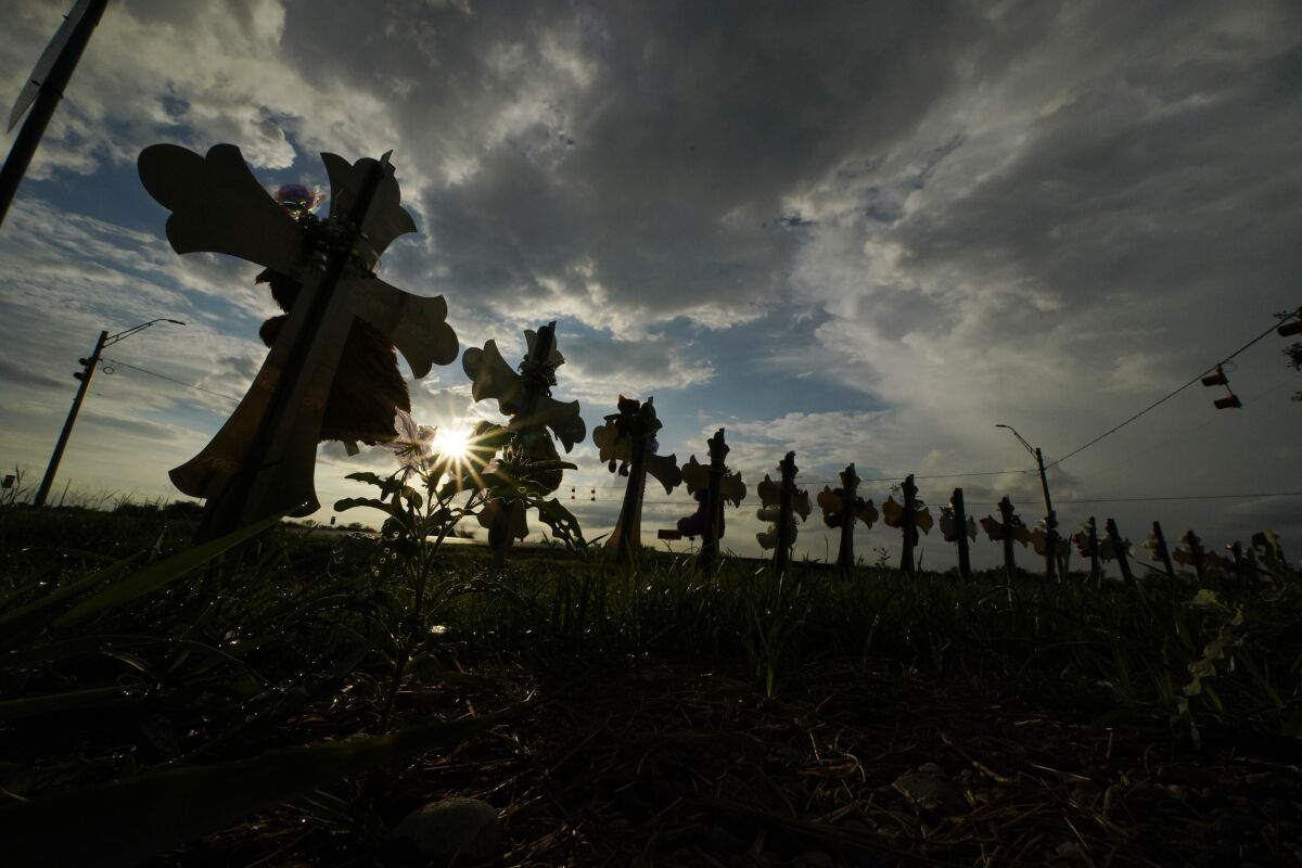 Vehicles pass crosses placed to honor the victims of the shootings at Robb Elementary School.