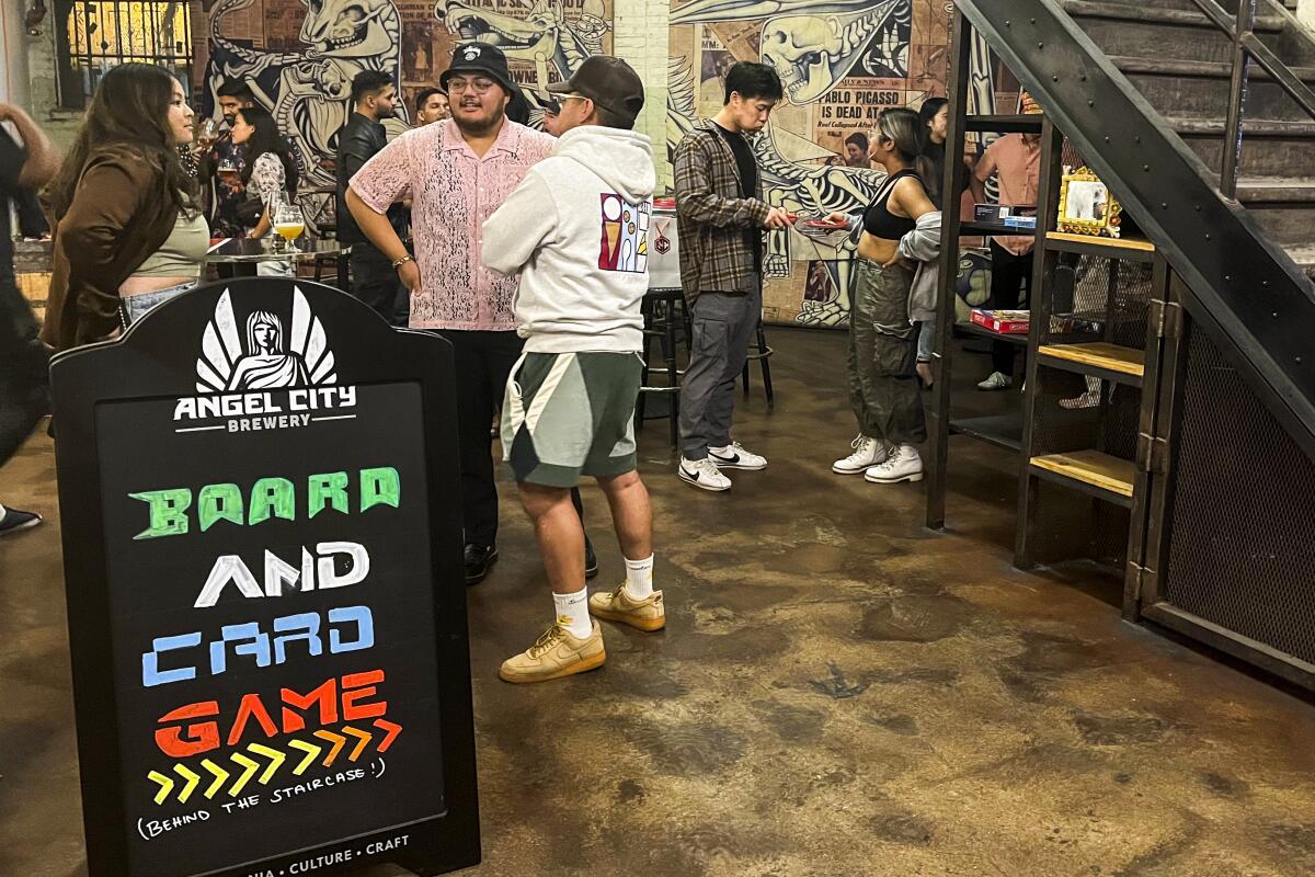 A group of people stand near a sign that says "Board and Card Game > (Behind the Staircase).