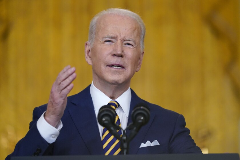 President Biden speaking into a microphone against a yellow backdrop