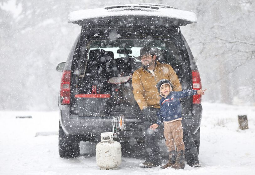 Craig Hodson of Campo and his son Leo warm up next to a propane heater as the snow fell in Mount Laguna as a storm moved through the area on Monday.