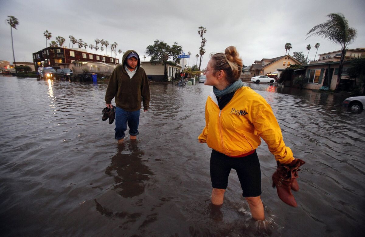 Shona Neufeld, right, and Johnathan Parker traverse West Point Loma Blvd in Ocean Beach away from their home near the flooding. — John Gastaldo / San Diego Union-Tribune