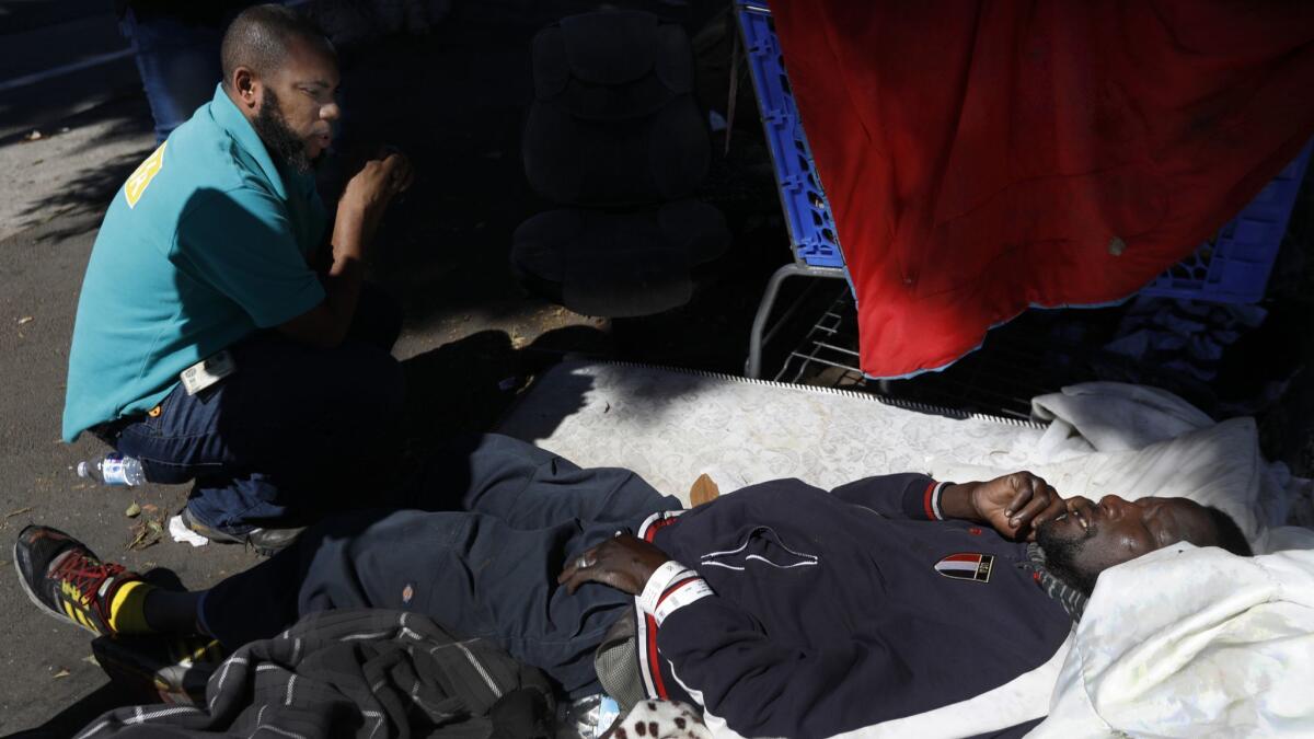 Outreach worker Geoffrey Goosby offers help to a man lying on a sidewalk mattress in south Los Angeles. The man declined help and refused to be taken to a hospital.