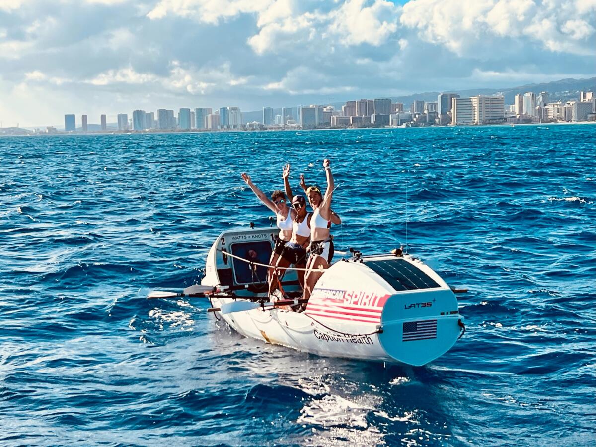 Four women stand on a rowboat and wave