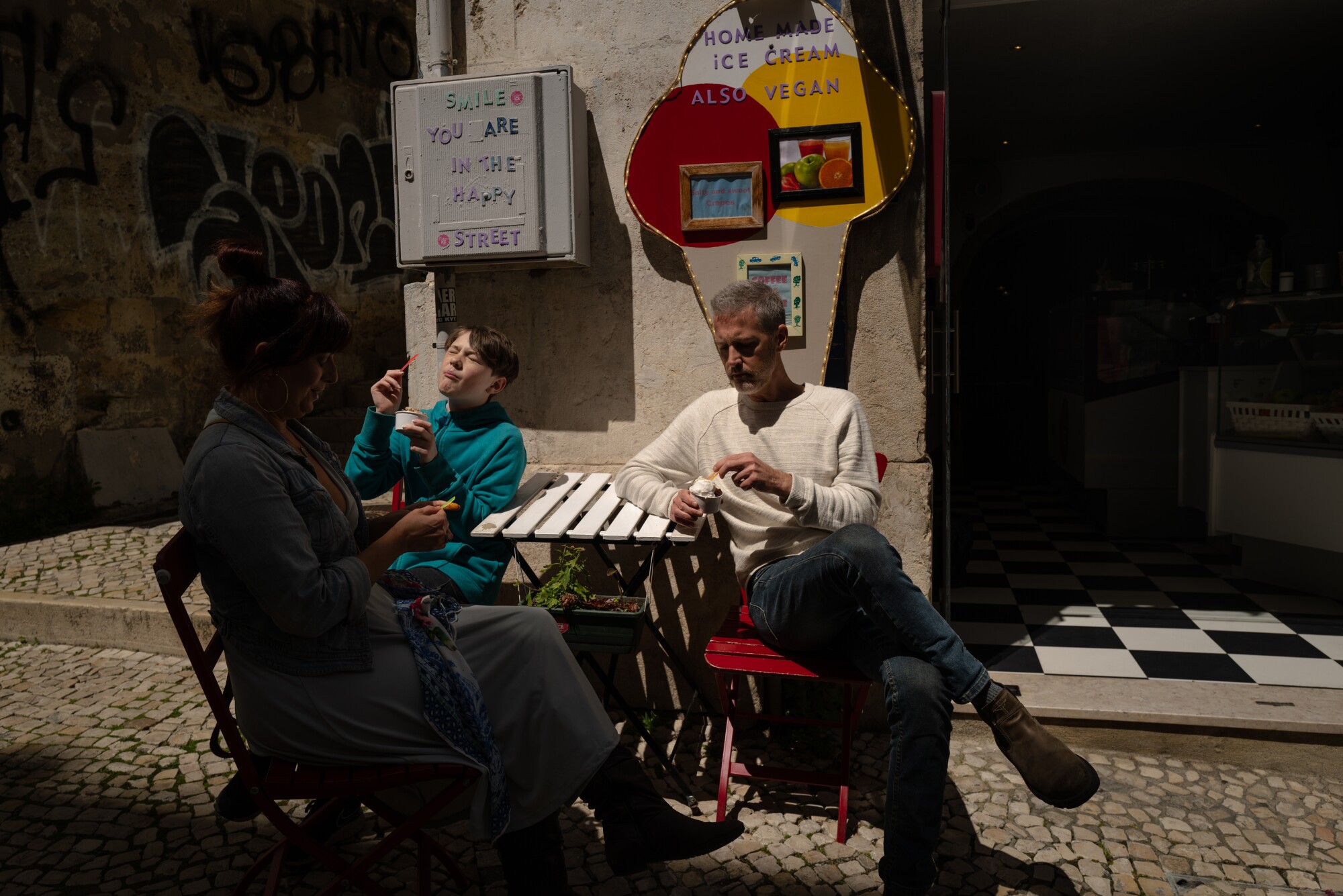 A woman, a man and a boy eat ice cream at a table outside a store